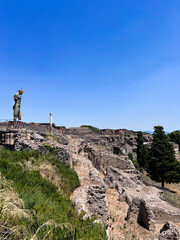 Ancient ruins under a clear blue sky with a lone statue. Pompeii, Italy.