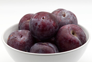 A close-up view of a bowl filled with fresh, ripe plums of varying shades of deep red and purple.