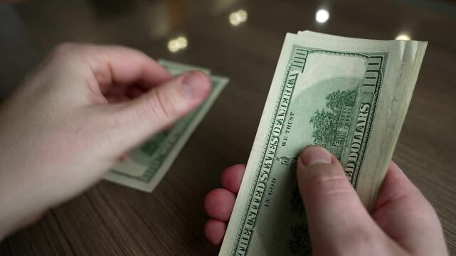 Hands are counting cash on a wooden table while discussing effective strategies for managing home finances. The focus is on practical methods for budgeting and tracking expenses.