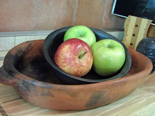 Two green apples and one red apple resting in black clay bowl