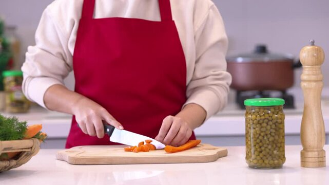 Close up view of male hands chopping carrot on wooden cutting board with knife	
