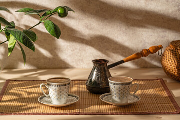Two cups of coffee and cezve on the table in the patio lit by morning sun.