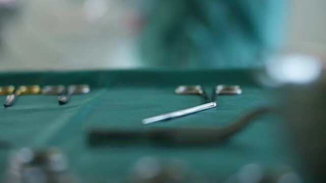 Close-up of surgical instruments on a sterile table in an operating room, with a gloved hand picking up tools. Concept of surgery preparation, medical precision, and healthcare professionalism