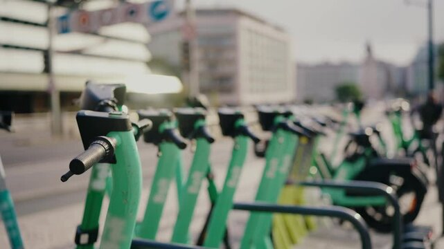 Close-up image of a row of green electric scooters parked in an urban setting on a sunny day, highlighting eco-friendly transportation and city commuting trends.