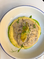 A creamy winter dish featuring tender stew over velvety mashed potatoes, garnished with pickles and microgreens, served in soft natural daylight