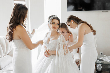 A bride is getting ready for her wedding with her bridesmaids. The bride is wearing a white dress...