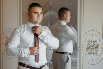 A man is getting ready for a formal event, putting on a tie and adjusting his shirt. Concept of...