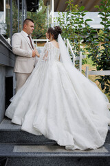 A bride and groom are standing on a staircase, the bride wearing a long white gown. The man is wearing a suit and tie. The scene is a wedding, and the couple is posing for a picture
