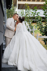 Naklejka premium A bride and groom are kissing on a staircase. The bride is wearing a long white gown and the groom is wearing a suit. Scene is romantic and intimate