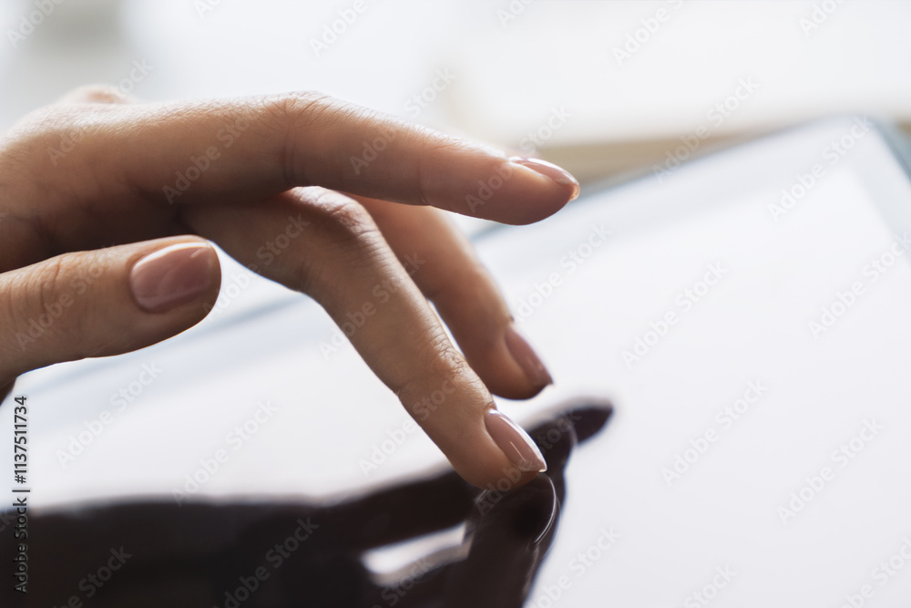 Poster closeup view of a woman's finger operating a high-tech tablet on a desk, amidst the blurred backdrop