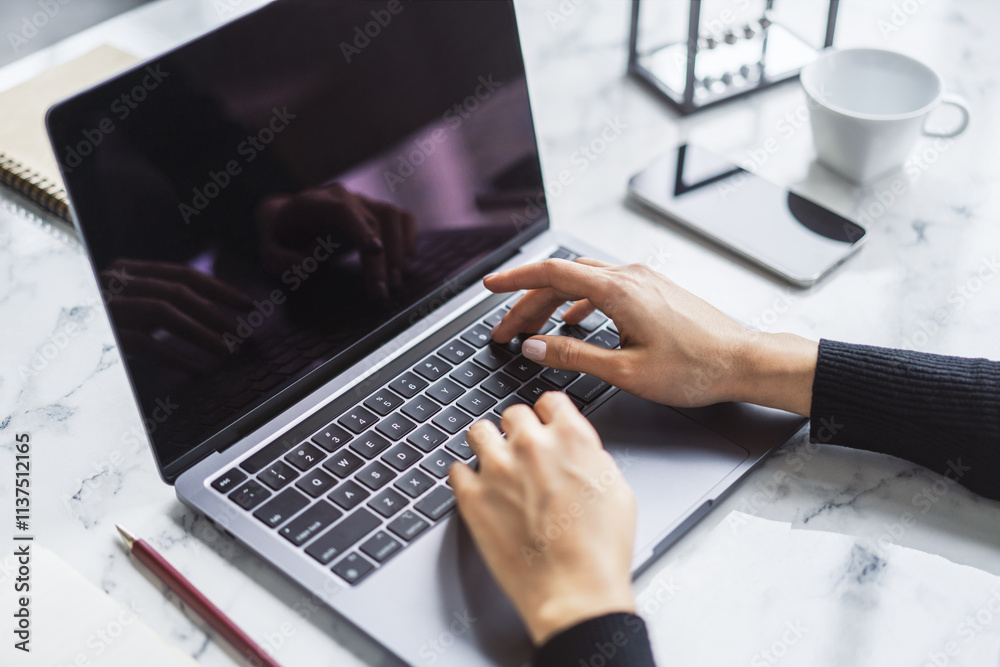 Poster a woman's hands typing on a sleek laptop keyboard, with the office environment appearing hazy in the