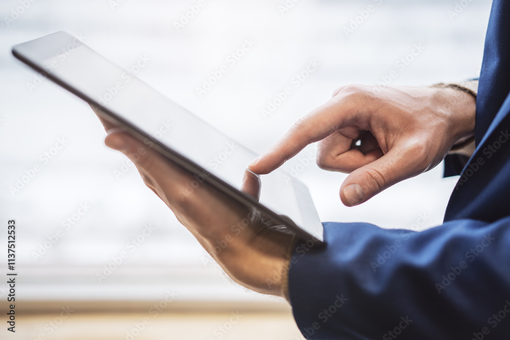 Poster close detail of a man's finger navigating the screen of an advanced tablet on a desk, set against th