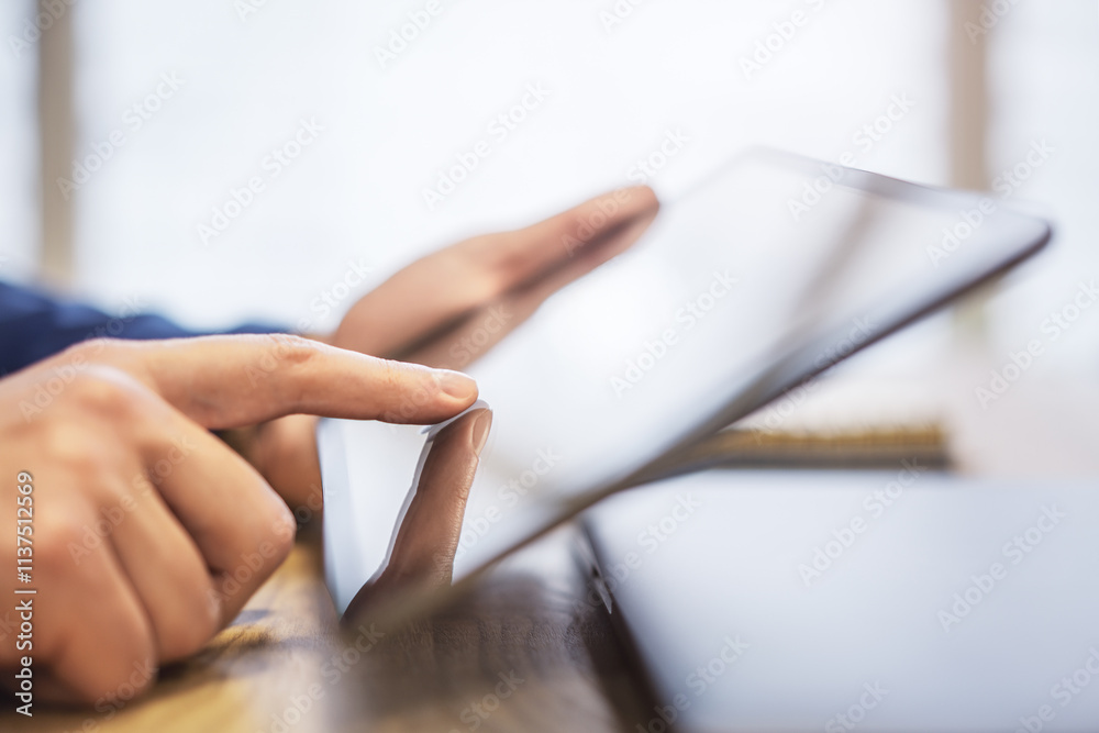 Poster man's finger touching a sleek digital tablet screen placed on a desk, within the softly lit blur of 