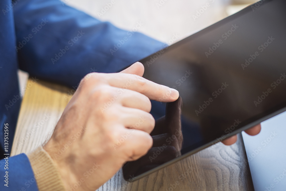 Poster man's finger touching a digital tablet screen placed on a desk, surrounded by the vague surroundings