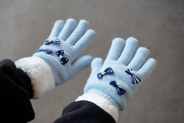 小学生の女の子向けの水色リボン付き手袋を、11歳の女の子が身につけている様子。