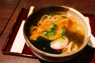 close up of hot udon noodles with seaweed, fishball and spring onion in a bowl in a wooden tray