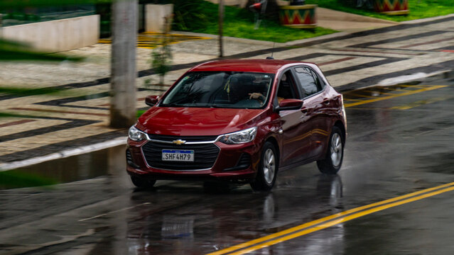 Red Chevrolet Onix in city street in the rain, Panning shot of hatchback in movement