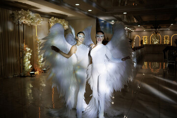 Two women dressed in angel wings are dancing on a stage. Scene is lighthearted and joyful, as the women are dressed in white and appear to be having fun © Vasil
