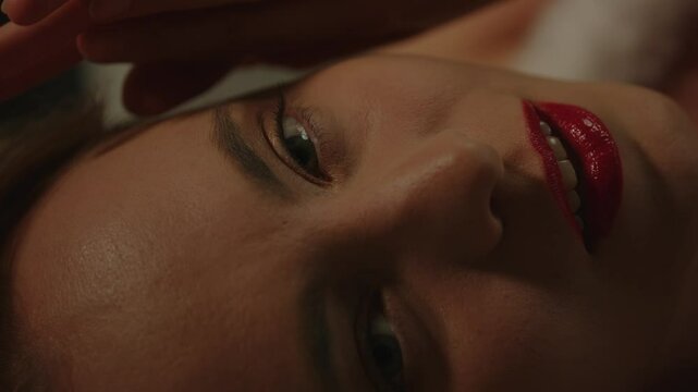 A seductive young woman wearing bright red lipstick sensually moans while looking at the camera