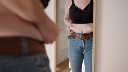 Overweight woman pinching her belly and looking herself in front of mirror
