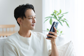 リビングのソファで携帯を持つ日本人男性