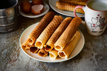 Sweet dessert for breakfast: Crispy waffle rolls on a white plate on a gray background. Close-up.