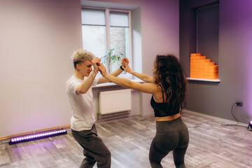 Slim young man and woman practicing salsa dance in training hall during group dancing classes