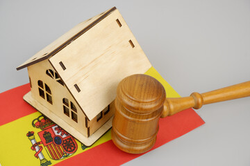 Law and real estate business in Spain. Judge gavel with wooden house model and Spanish flag on gray...
