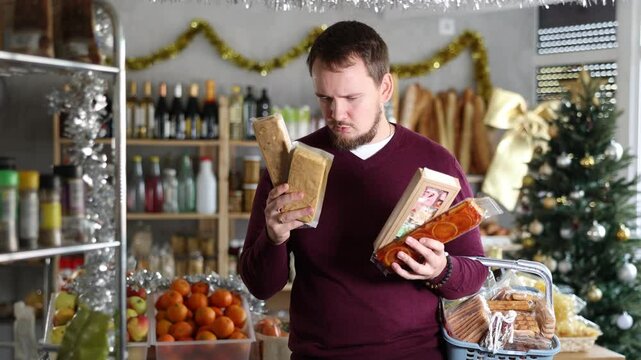 In festive little store decorated with Christmas tree and shiny tinsel, smiling young man with beard browsing shelves, picking out rich nutty turron and imagining joy of indulging in sweet delight