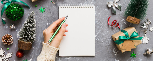 Woman writing Christmas to do list on notebook on colored background with xmas decorations