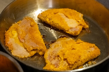 Crispy fried fish fillets cooking in a skillet with a golden crust and sizzling oil
