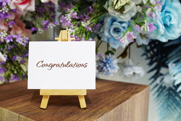 Congratulations text write on paper card with wooden easel and flowers decoration on wooden background