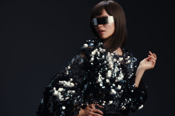 Woman posing in sunglasses and sequinned jacket, against a black background, creating a stylish, glamorous look