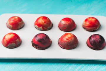 Assorted multi-colored homemade chocolates. Modern hand-painted chocolates on a white plate on a blue background. copyspace.Product concept for chocolatier. Selected focus.