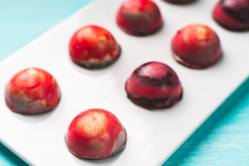 Assorted multi-colored homemade chocolates. Modern hand-painted chocolates on a white plate on a blue background. copyspace.Product concept for chocolatier. Selected focus.