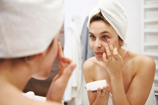 Mirror image of young woman applying moisturizer in bathroom