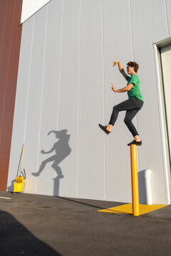 Acrobat standing on pole, casting shadow at cleaning bucket