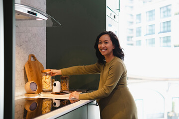 Smiling pregnant woman taking jar from table in modern kitchen at home