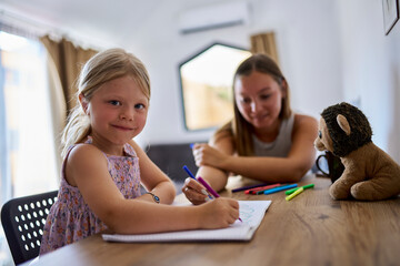 Smiling girl drawing on paper with mother at table