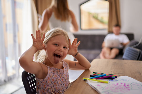 Girl teasing and drawing with felt tip pens near parents at home