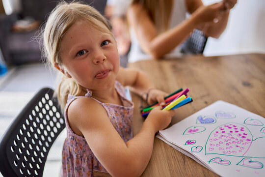 Smiling girl holding multi colored felt tip pens and drawing heart shapes on paper