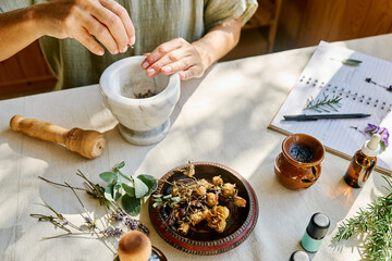 Woman preparing for aromatherapy session with essential oil diffuser and medical herbs at home
