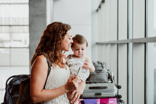 Smiling mother carrying baby daughter and holding passport at airport