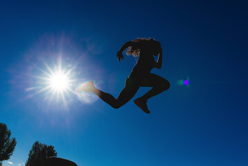 Sportive young woman jumping under blue sky in backlight