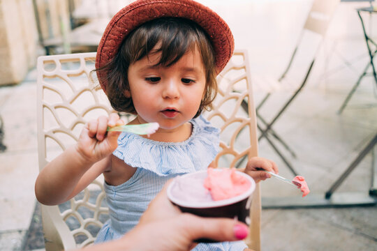 Cute toddler girl eating an ice cream held by her mother