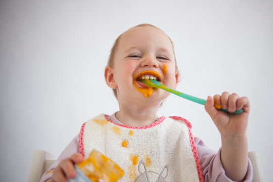 Portrait of funny baby girl eating mush