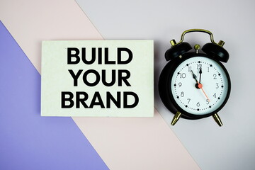 Build Your Brand text on paper card with alarm clock on purple and pink geometric background