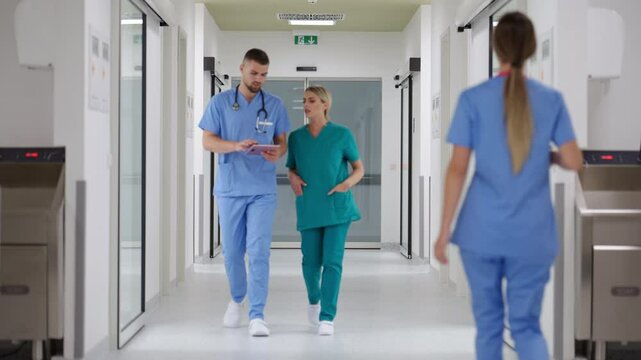 Medical professionals walking through a hospital corridor, discussing patient care and reviewing notes on a digital tablet. Concept of teamwork and collaboration in healthcare settings