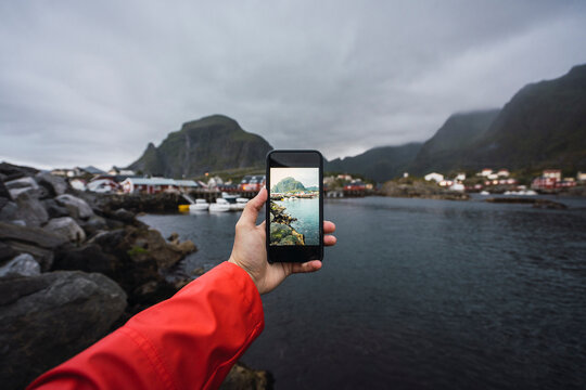 Norway, Lofoten, man's hand taking cell phone picture at the coast