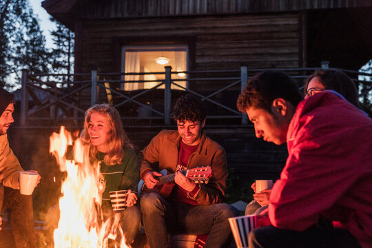 Group of friends sitting at a campfire, talking and playing guitar - Powered by Adobe